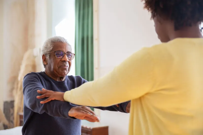 Elderly man with a caregiver assisting him in exercise at home